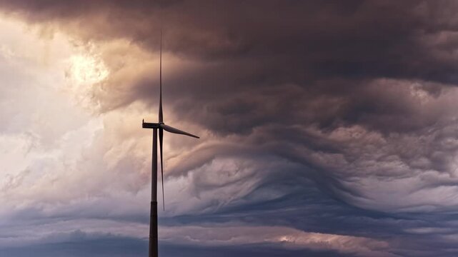 Aerial view of a single wind turbine standing against a dramatic, dark, and stormy sky in Latvia.