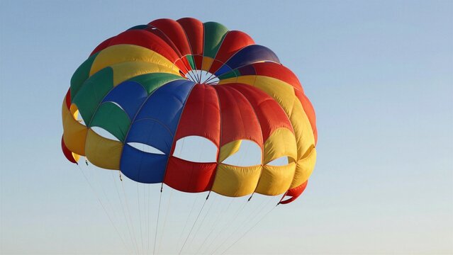 A colorful parasail canopy glides gracefully through a calm, cloudless sky during a bright sunny day.