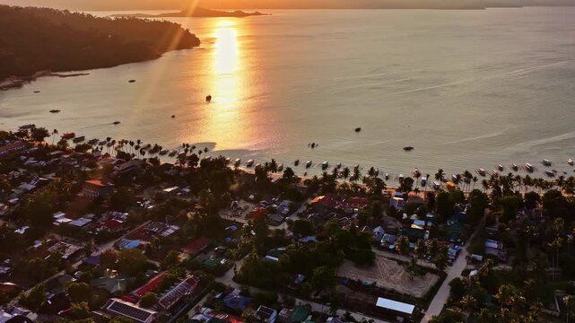Aerial view of Port Barton Beach at sunset with traditional outrigger boats moored along the shore and golden light reflecting on the water in Mimaropa, Philippines.