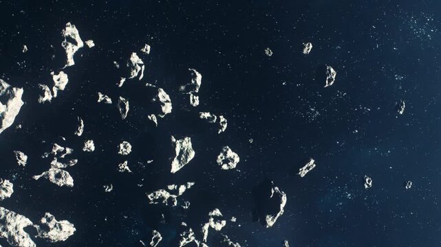 Rocks float in a vast space filled with stars. This scene shows an asteroid field with many different shapes and sizes of asteroids moving slowly.