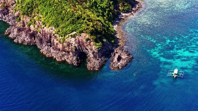 Aerial view of Port Barton Beach featuring rocky cliffs, lush green vegetation, and a traditional outrigger boat floating in turquoise water in Mimaropa, Philippines.