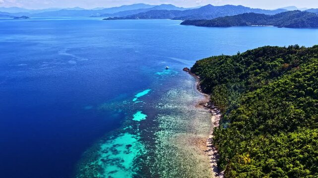 Aerial view of Port Barton Beach with lush tropical forest, turquoise coral reefs, and deep blue sea in Mimaropa, Philippines.