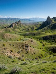 Fototapeta premium Rolling green hills meet jagged rocky peaks under a clear blue sky. A town rests in the valley below distant snow capped mountains. Nature raw beauty.