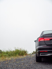 Dark car parked on gravel road under bright sky. Minimalist composition highlights vehicle's sleek lines. Perfect for automotive, travel, or modern lifestyle themes © mark_gusev