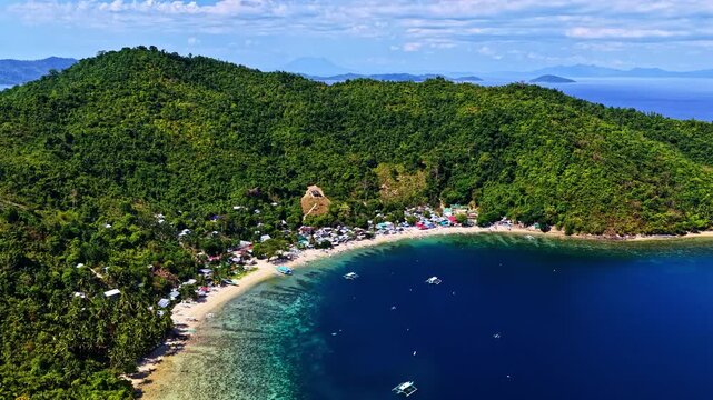 Aerial view of Port Barton Beach with lush green hills and small boats in the clear blue water of Mimaropa, Philippines.