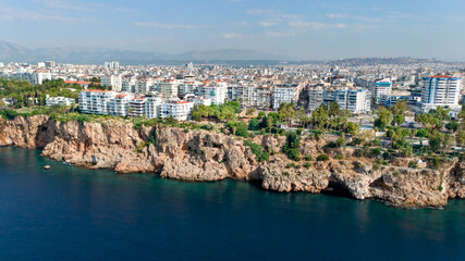 Obraz premium Aerial panorama of Antalya city above rugged Mediterranean sea cliffs with dense urban buildings and distant mountains in Turkey