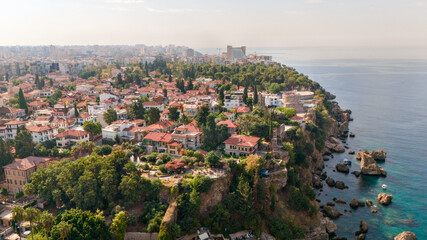Obraz premium Aerial view of Antalya's Kaleici old town with red tile houses, Hidirlik Tower, lush park and rugged Mediterranean coastline