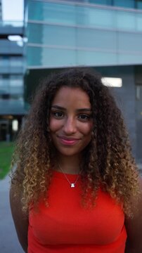 Vertical. Trendy young woman with curly hair and vibrant smile standing in a modern city street, ideal for social media, youth fashion, or lifestyle branding visuals.