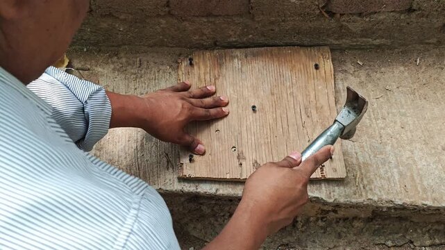 Handyman Hammering Screws into Wooden Base Board Close Up