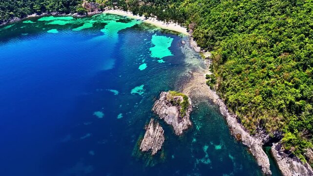 Aerial view of Port Barton Beach featuring turquoise waters, rocky outcrops, and lush tropical forest along the coastline in Mimaropa, Philippines.