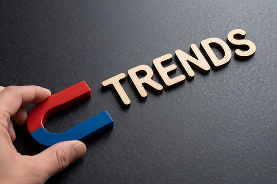Hand holding magnet lifting wooden block spelling trends on dark background