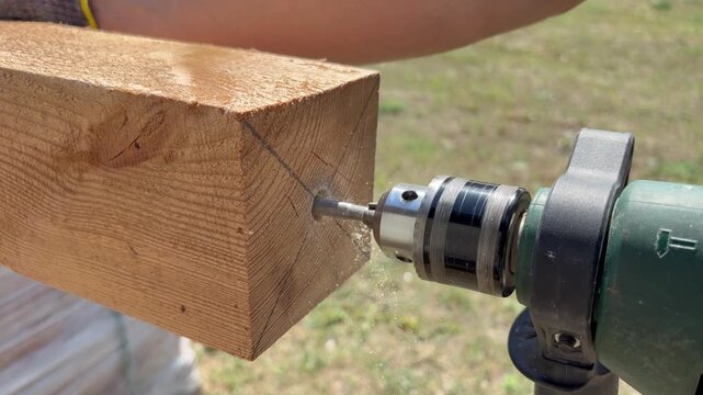 Drilling hole in wooden beam with drill from below outdoors. Construction work, DIY projects