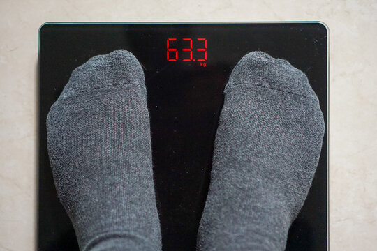 Gray socks rest on a digital scale. Red display shows weight: 63.3. No face or expression visible. Health, fitness, or weight tracking theme. Ideal for wellness or lifestyle content