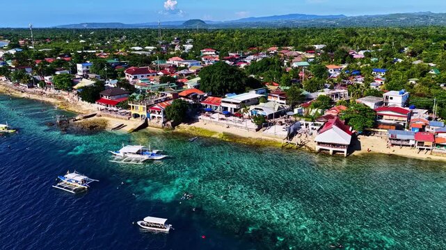 Aerial view of the coastal town of Moalboal with turquoise waters, traditional outrigger boats, and buildings along the shoreline in Moalboal, Central Visayas, Philippines.
