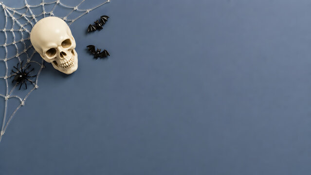 Halloween flat lay with skull and spider web. Spooky holiday background with bats and copy space. Dark blue festive composition.