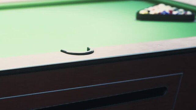 A group of friends enjoys a game at a pool table inside a bar. The green felt and wooden edges stand out in the evening light. Laughter and conversation fill the air.