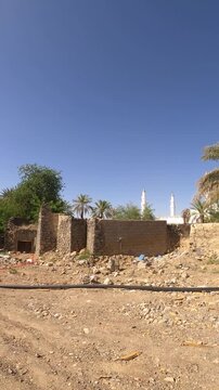 Distant view of Masjid Quba minarets behind old stone ruins and palm trees in Medina.