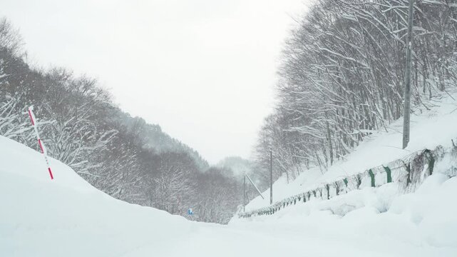 Point of view by windshield of Driving car on a snow-covered mountain road with pine tree forest in snowy day. Beautiful scenic nature countryside and transportation in winter season.