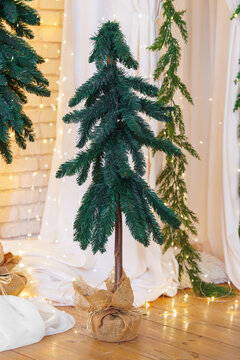 Small artificial Christmas tree decorated with warm fairy lights and burlap, creating a cozy festive atmosphere for winter holiday celebrations. Rustic aesthetic decor, holiday mood