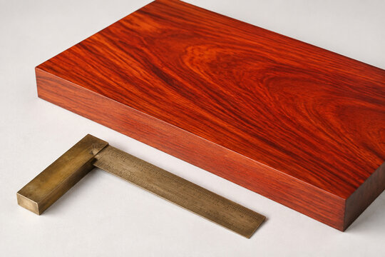 Polished padauk wood slab with brass carpenter's square, bright studio surface, wide crop