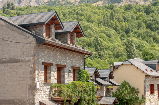 The stone architecture and slate roofs of a traditional Pyrenees mountain village nestle among green forested mountains near Hoz de Jaca Spain in summer a charming image of timeless rural life.