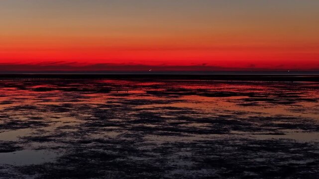 Aerial view of tidal flats at sunset with vibrant orange sky reflecting on the water surface in Eemshaven, Groningen, Netherlands.