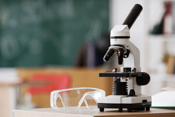 Naklejka premium Science education and research, microscope and safety goggles on a classroom desk for biology study and laboratory experiment in a school environment