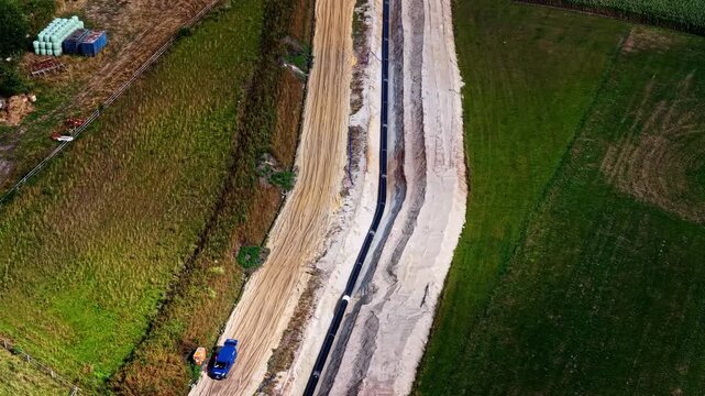 Aerial view of the pipeline construction site at ZE PAK SA Elektrownia Patnow with a black pipe in a sandy trench and a blue vehicle nearby in Konin, Wielkopolskie, Poland.