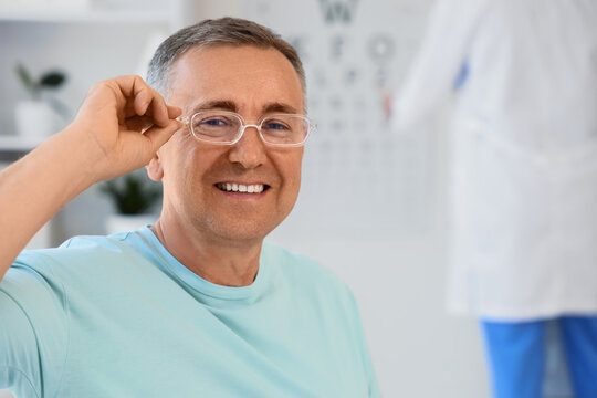 Vision care and eye health, mature man testing new prescription glasses at an optometrist clinic with a blurred eye chart in the background