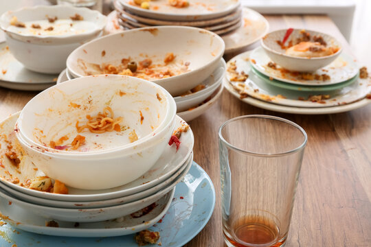 Food waste and household chores, stack of dirty dishes with leftover food and empty glass on a wooden table after a messy dinner party at home