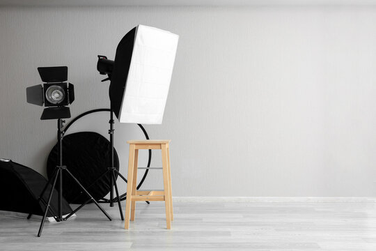 Photography studio setup, professional lighting equipment and wooden stool for portrait session in empty room with copy space for creative production