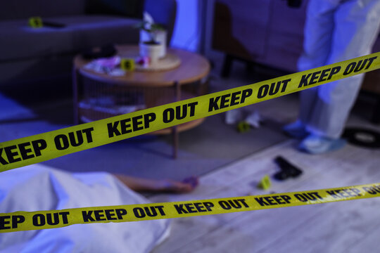 Crime scene investigation and forensic evidence, police tape blocking access to a residential room with a body and a handgun on the floor