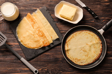 Obraz premium Frying pan with tasty thin pancakes, spatula, knife and ingredients on wooden background