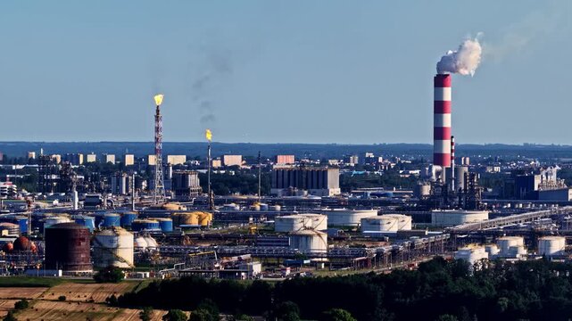 Aerial view of Orlen Plock Production Plant with industrial chimneys, storage tanks, and flare stacks under a clear blue sky in Plock, Mazowieckie Voivodeship, Poland.