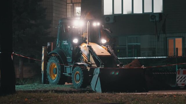Backhoe Loader Digging with Bright Headlights at Night | Excavator Front Bucket Loading Soil Near Building | Urban Construction Site with Warning Tape