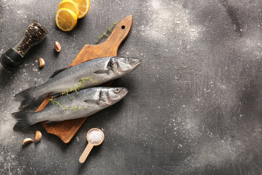 Wooden board with fresh raw seabass fishes and different spices on dark background