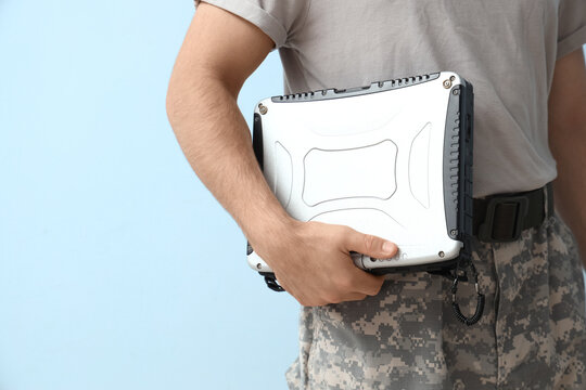 Young soldier with military laptop on light background, closeup