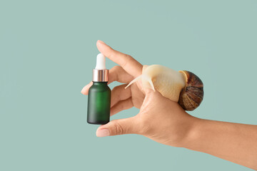 Female hand with snail and bottle of serum on green background © Pixel-Shot