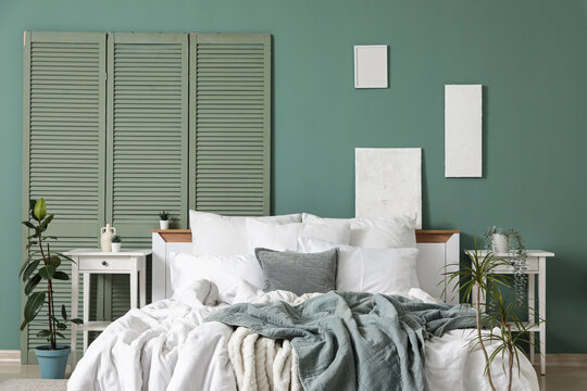 Big comfortable bed, folding screen and bedside tables near green wall in bedroom, closeup