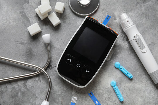 Glucometer with lancet pen, test strips, sugar cubes and stethoscope on grey grunge background
