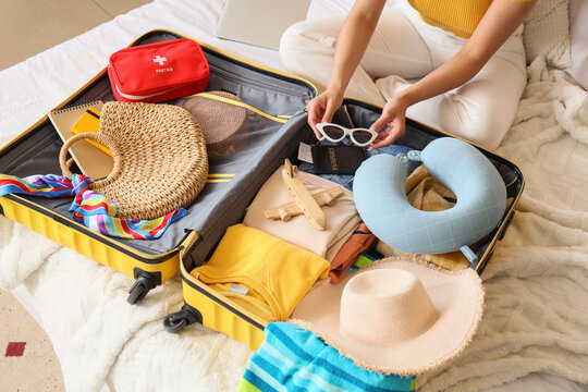 Young woman packing travelling accessories into suitcase in bedroom