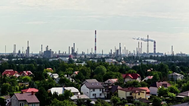 Aerial view of ORLEN Plock Production Plant with industrial chimneys and smoke rising above residential houses and green trees in Plock, Mazowieckie, Poland.
