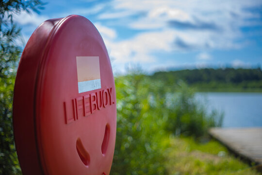 Red plastic lifebuoy housing container mounted near a calm lake dock under a cloudy sky