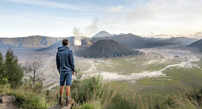 Young man in front of volcanic landscape, view in Tengger Caldera, smoking volcano Gunung Bromo, in front Mt. Batok, behind Mt. Kursi, Mt. Gunung Semeru, National Park Bromo-Tengger-Semeru, Java, Indonesia