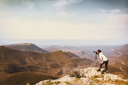 Young passionate attractive caucasian hipster woman content creator photographing mountains with red girly DSLR camera on tripod. Georgia