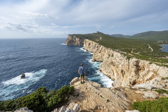 Tourist enjoying the view of steep cliffs by the sea, coastal landscape, cliffs on the Capo Caccia headland, Alghero, Sardinia, Italy