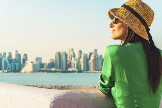 Woman traveler visitor standing at waterfront enjoy Doha skyline viewpoint across bay symbolizing freedom urban lifestyle travel Middle East modern city concept