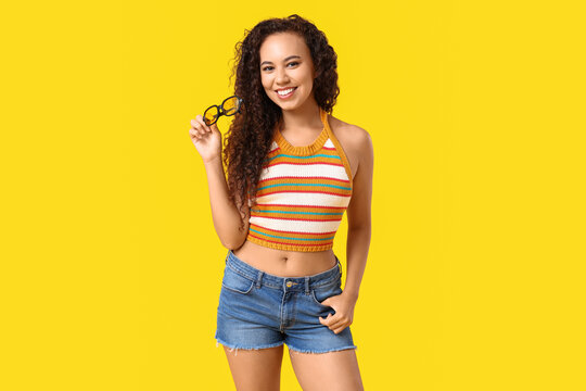 Beautiful African-American woman with sunglasses on yellow background