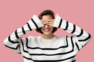 Obraz na płótnie Canvas Beautiful young woman in stylish striped sweater closing her eyes on pink background