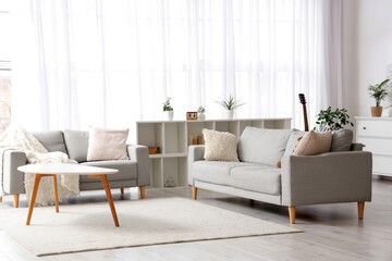Interior of light living room with grey sofas, table and shelf unit